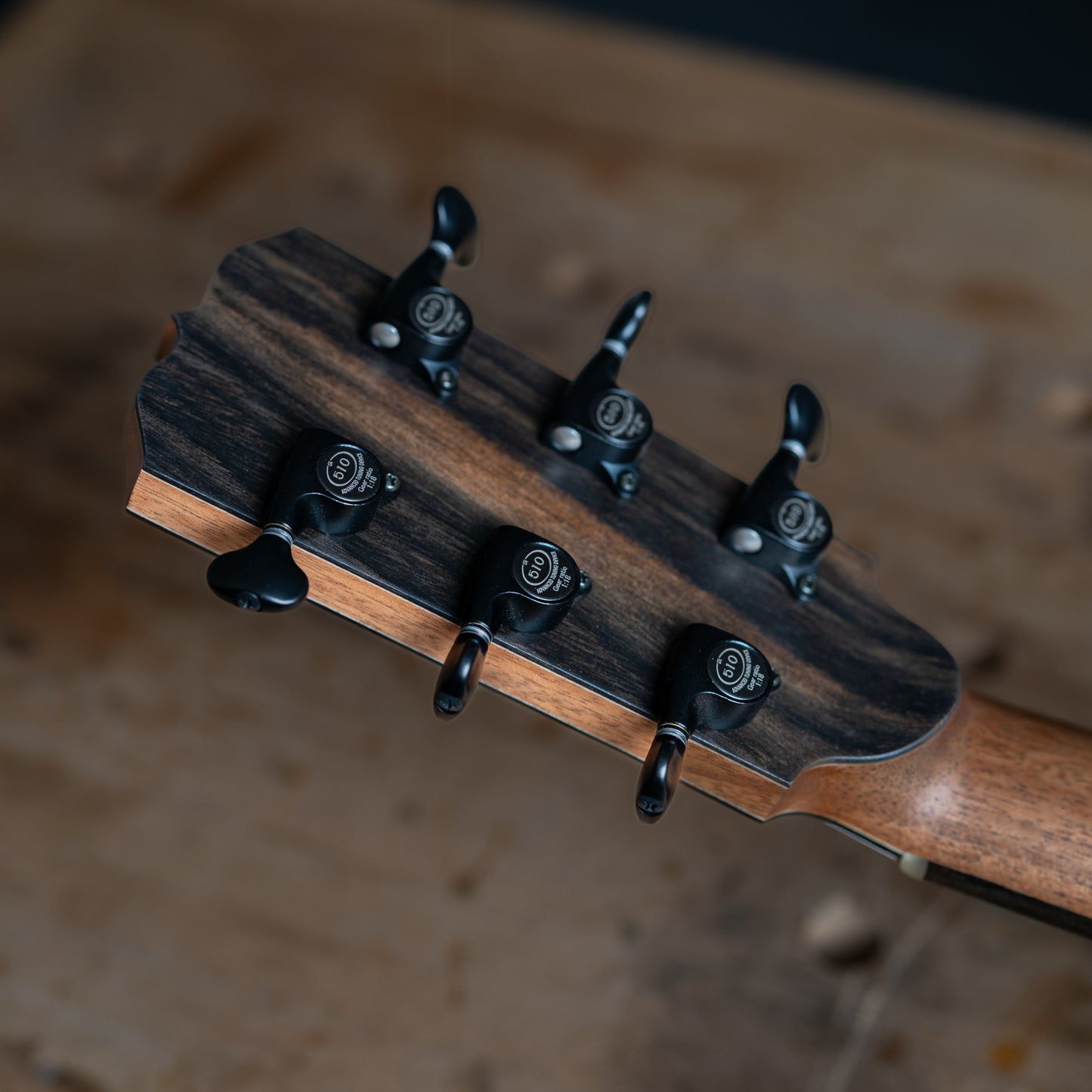 Close-up of a guitar headstock with tuning pegs on a wooden surface