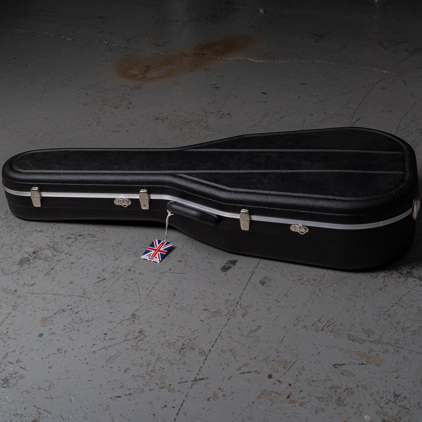 Black guitar case on a gray floor with a small Union Jack flag attached.